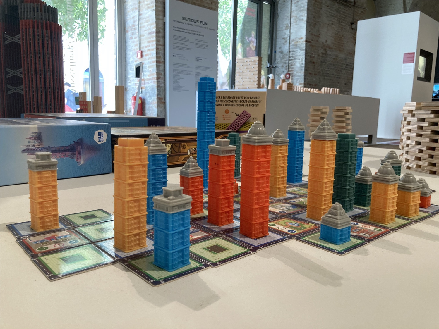 Eingangsbereich der Ausstellung Serious Fun, Detailaufnahme, im Vordergrund ein Brettspiel, bei dem auf quadratischen Karten auf dem Tisch Türme in unterschiedlichen Farben und Größen aufgebaut sind