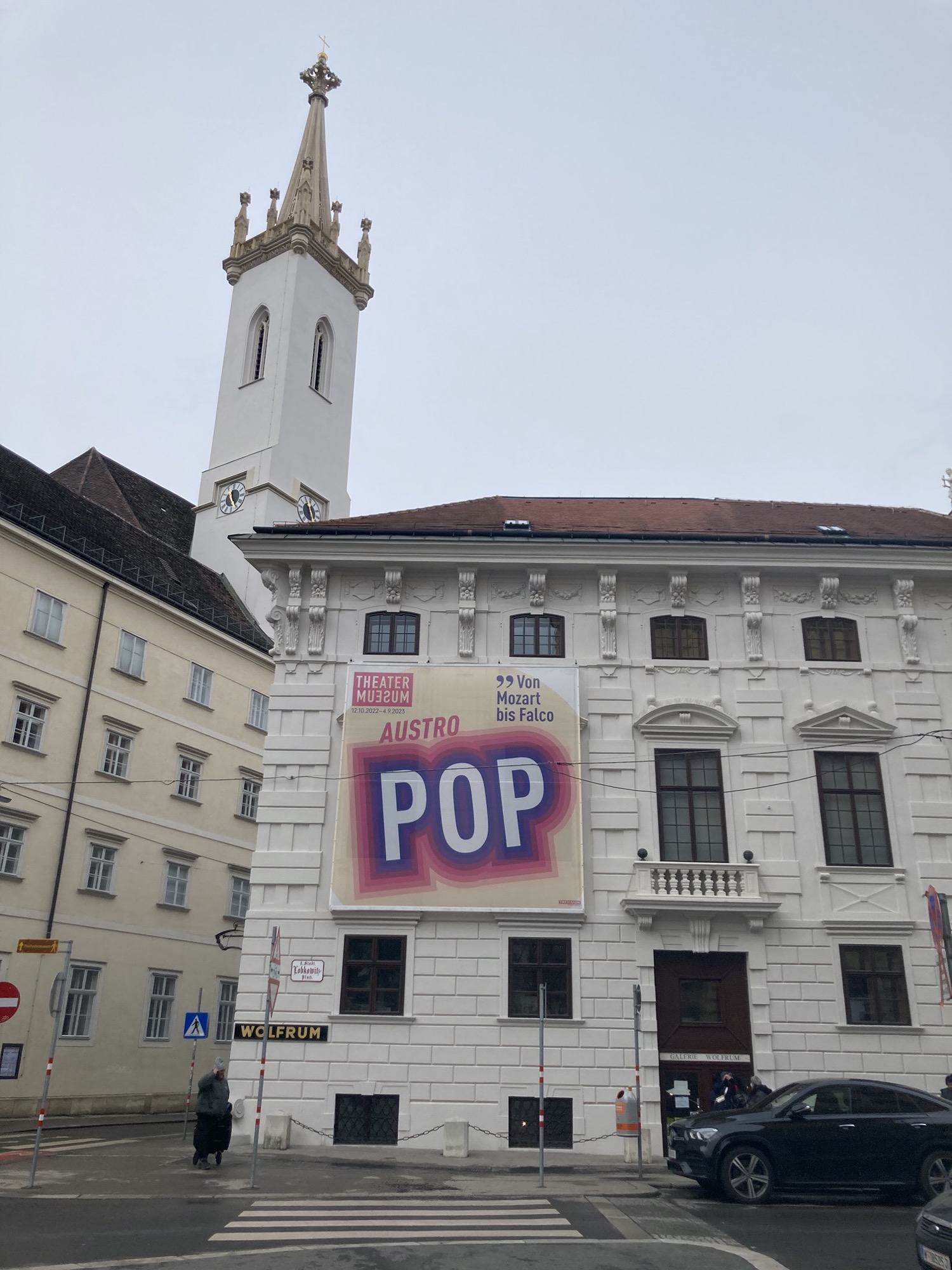 Theatermuseum mit dem bunten Plakat zur Ausstellung Austropop, dahinter der Kirchturm der Augustinerkirche