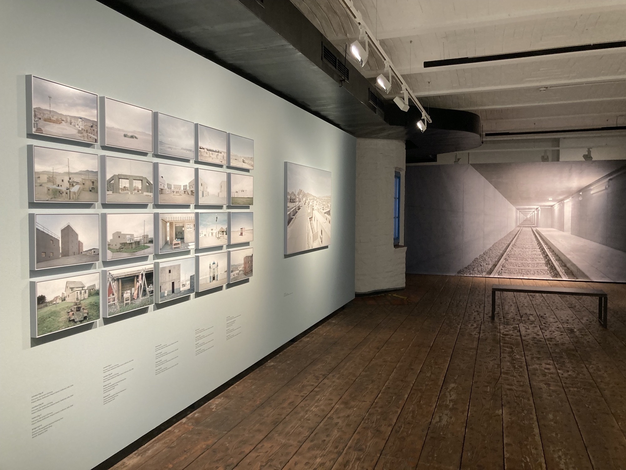 Blick in den Ausstellungsraum, links eine Collage aus 4x5 Bildern aus der Serie The Potemkin Village, hinten ein wandfüllender Blick in einen U-Bahn-Schacht aus der Reihe Subspace