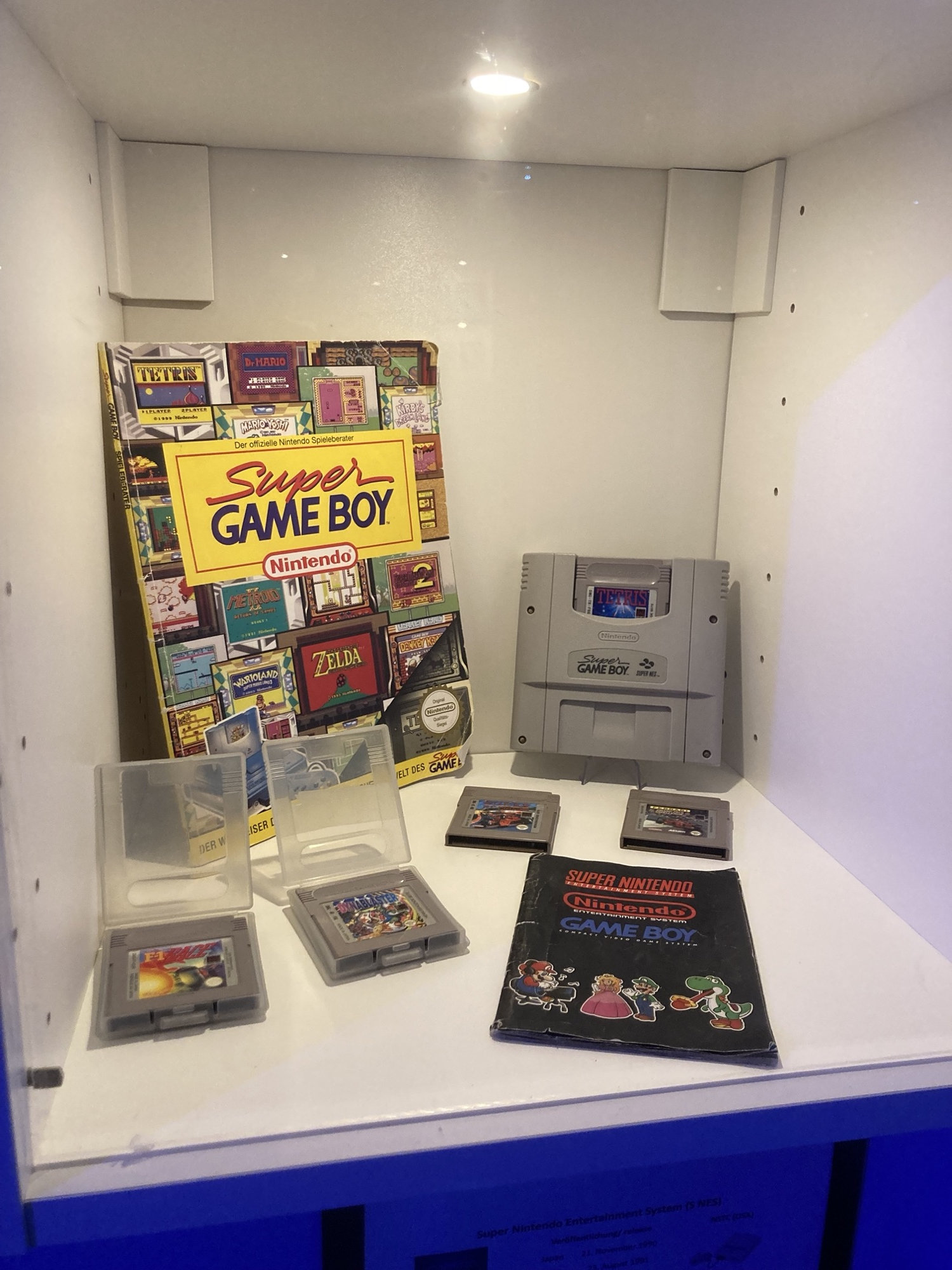 ein Display, das verschiedene Game Boy Spielekassetten zeigt, daneben die Adapterkassette, die es erlaubt Game Boy Spiele auf dem Super NES zu spielen sowie ein Lösungsheft für diverse Game Boy Spiele aus der Pre-Internet-Ära