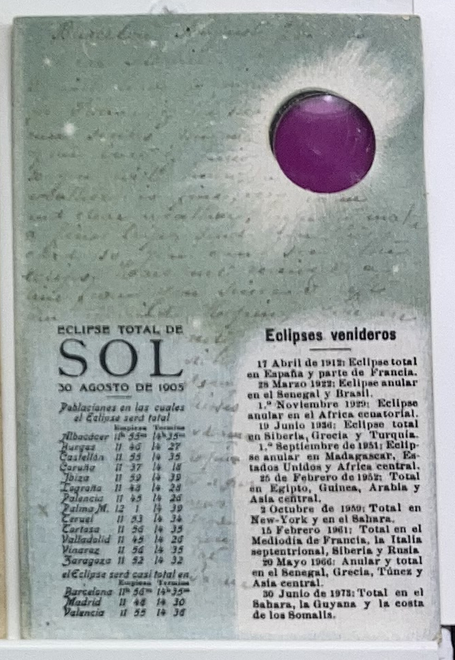 Postkarte anlässlich der totalen Sonnenfinsternis (Eclipse Total de Sol) am 30. August 1905, in der linken Textspalte sind die Uhrzeiten aufgelistet, an denen die Sonnenfinsternis an verschiedenen Orten zu sehen ist, in der rechten Spalte eine Auflistung von prognostizierten Eklipsen in späteren Jahren, der Hintergrund ist ein Text in Schreibschrift auf grauem Papier, rechts oben ein runder Ausschnitt mit einem Filter, durch den die Sonne betrachtet werden kann