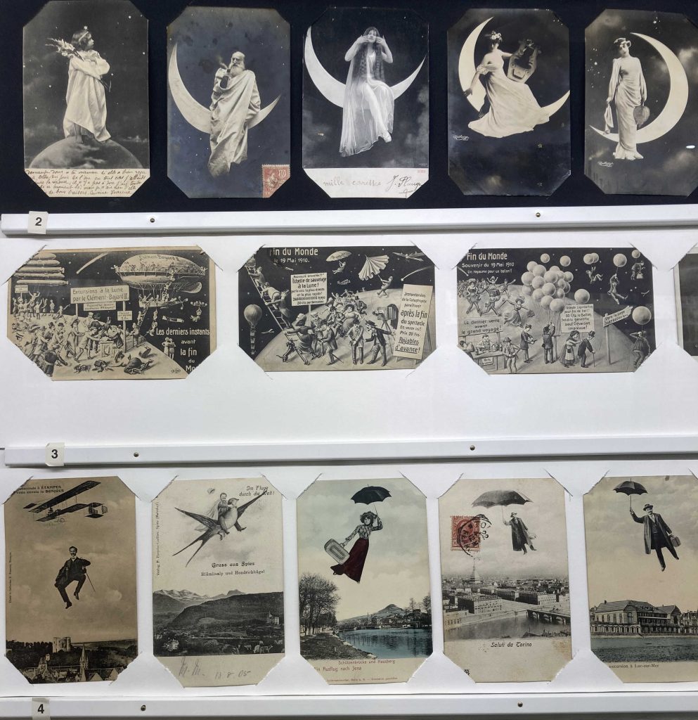 3 Reihen von Postkartenmotiven, oben verschiedene menschliche Gestalten, die vor einem Weltallhintergrund abgebildet sind und auf dem Mond stehen oder sitzen, mittig querformatige Illustrationen von Menschenmengen auf Planeten, die das Ende der Welt feiern, unten hochformatige Ansichten, die Menschen in der Luft schwebend zeigen, einer reitet auf einem übergroßen Vogel, rechts schweben drei Personen an Schirmen über einem Stadtbild mit Fluss