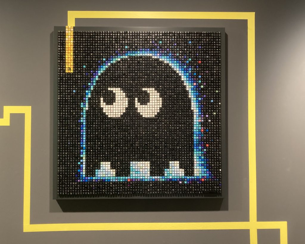 Pixelbild eines Geists aus dem Computerspiel Pac-Man, das Bild ist hauptsächlich schwarz, die Konturen des Geists bestehen aus unterschiedlichen Blautönen, die Augen schauen nach links, bei genauerem Hinsehen wird deutlich, dass das Bild aus einzelnen Buchstaben von Computertastaturen zusammengesetzt ist