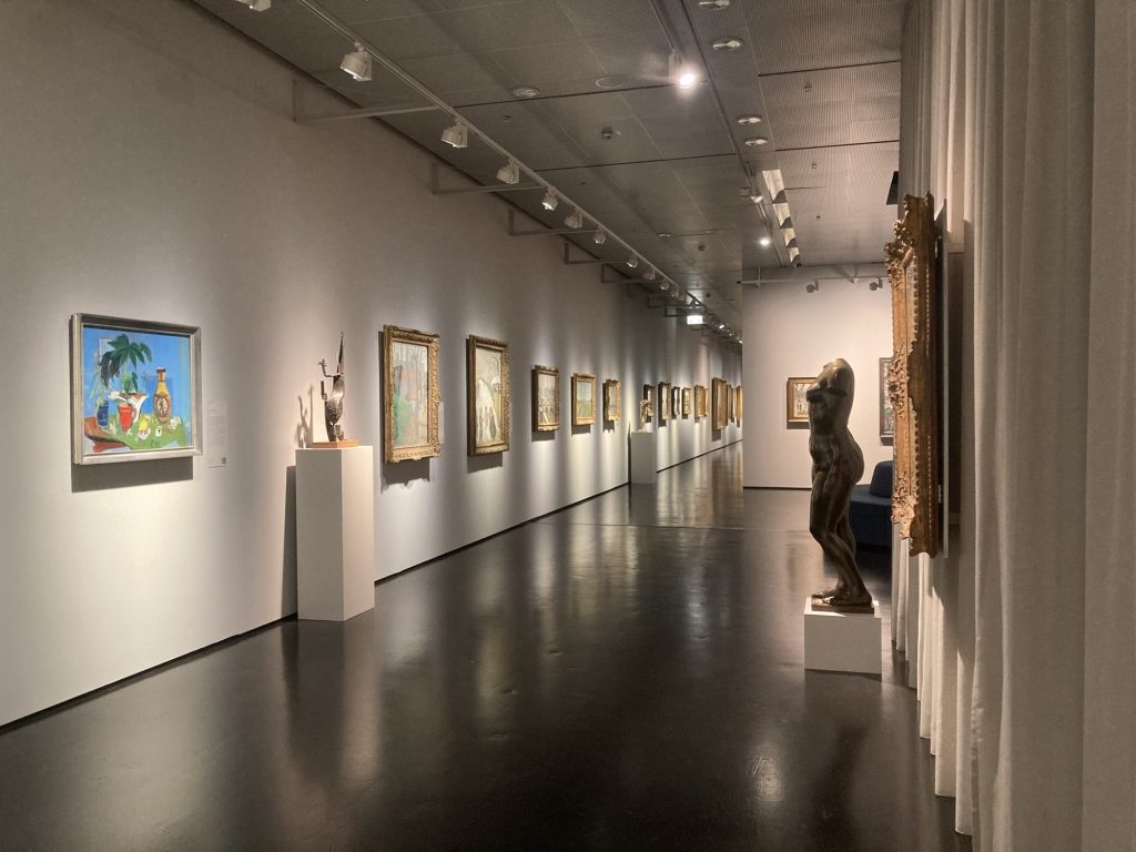 Blick in den modernen Teil der Ausstellung, links ein modernes Bild in einem schlichten Rahmen neben einer Skulptur, die einem Kaktus ähnelt, dahinter im Raum eine Reihe an Bildern in dekorativen Goldrahmen, rechts im Vordergrund ebenfalls ein Bild in einem dekorativen Goldrahmen, daneben eine Skulptur eines menschlichen Körpers ohne Kopf