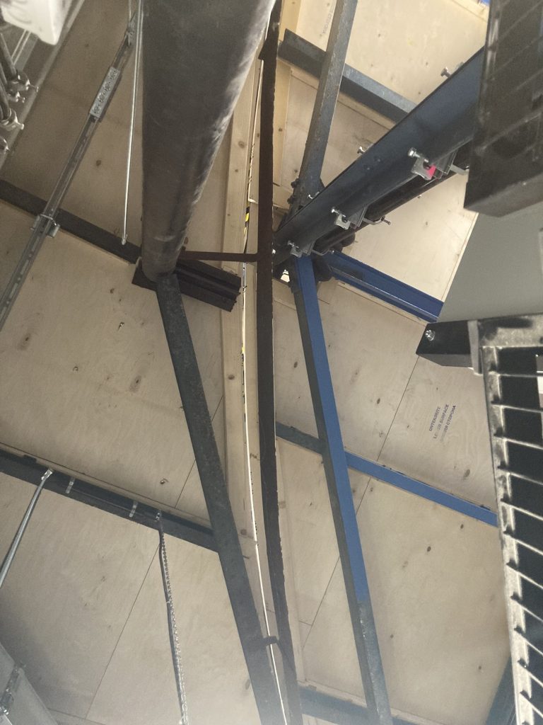 Blick von unten auf die Drehbühne, die Schnittkante des Bühnenzylinders ist deutlich zu sehen, der innere Bereich, der sich mitdreht, wird von blauen Stahlträgern gehalten, der äußere Bereich ist mit schwarzen Stahlträgern versehen